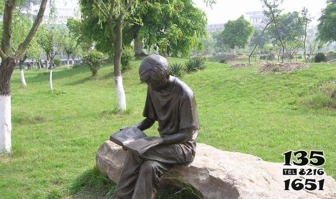 读书雕塑-公园草坪玻璃钢仿铜坐着石头上的男孩读书雕塑高清图片