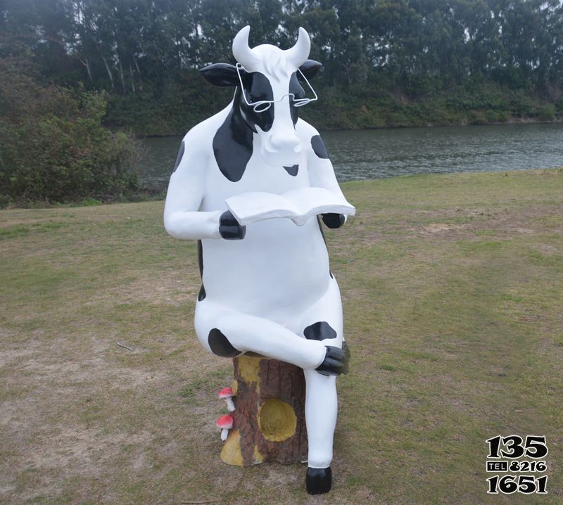 牛雕塑-公园中一只坐着看书的玻璃钢牛雕塑高清图片